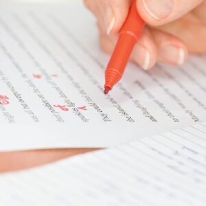 A person writing on paper with red pen.