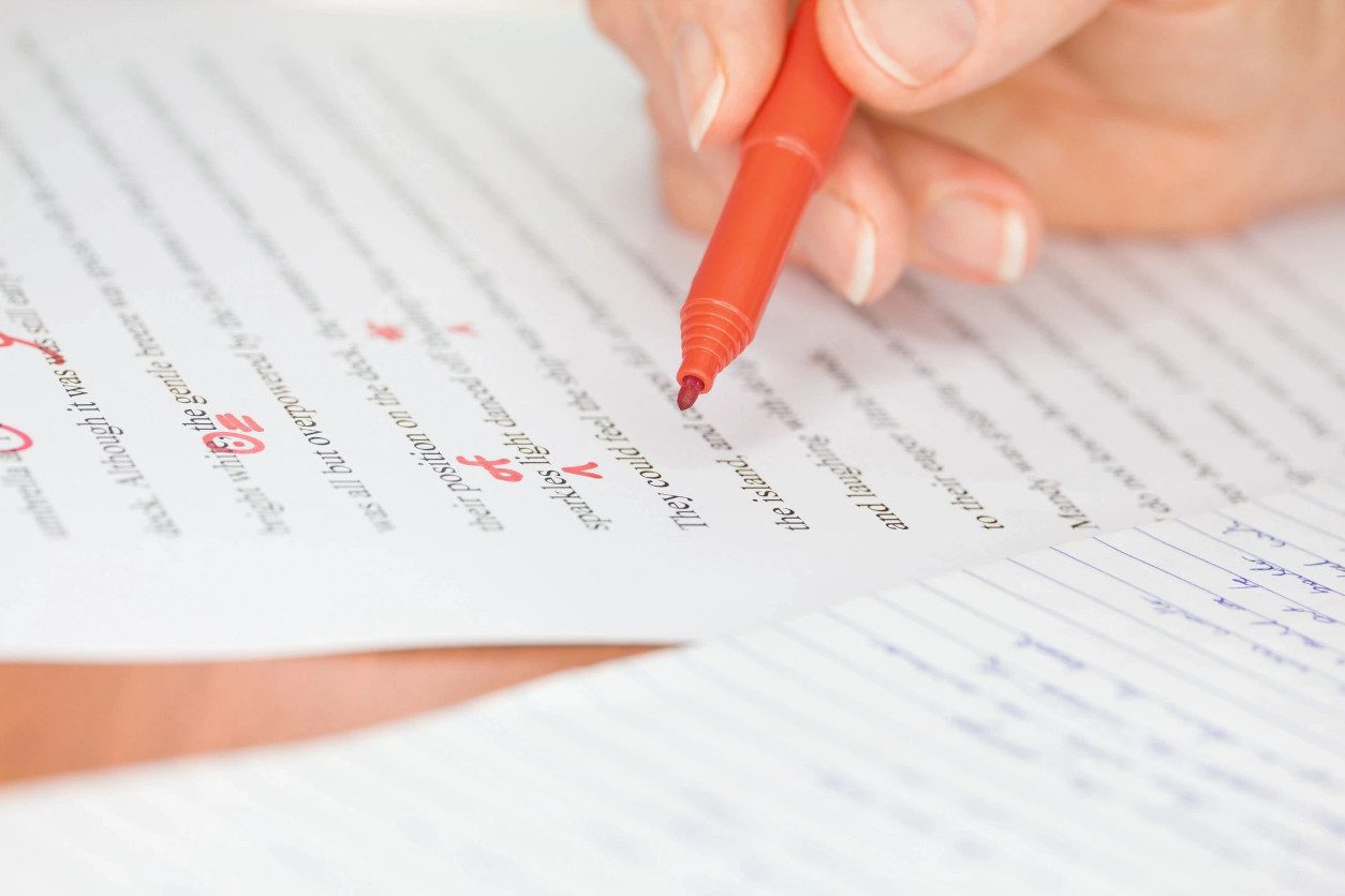 A person writing on paper with red pen.